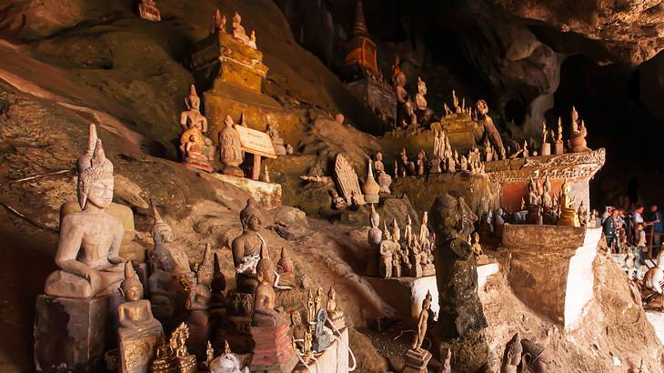 Many Buddha statues in various poses scattered around the inside of a cave