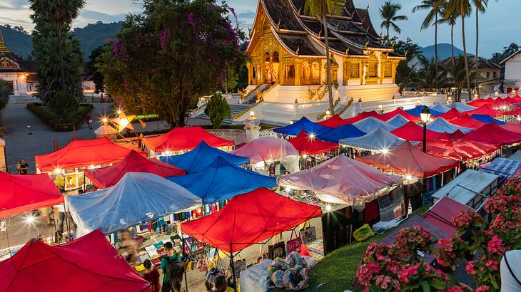 Rows of colourful tents with merchandise and people in front of a golden temple