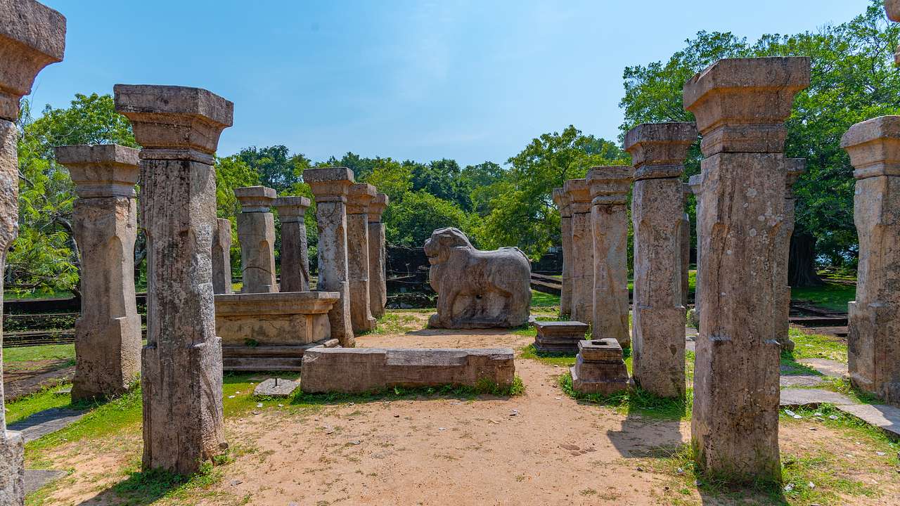 A lion statue surrounded by pillars and green trees