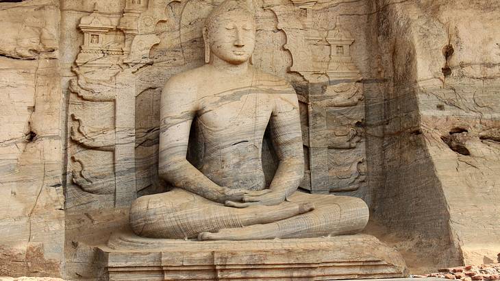 A large statue of a Buddha with sitting on a platform carved on a rock