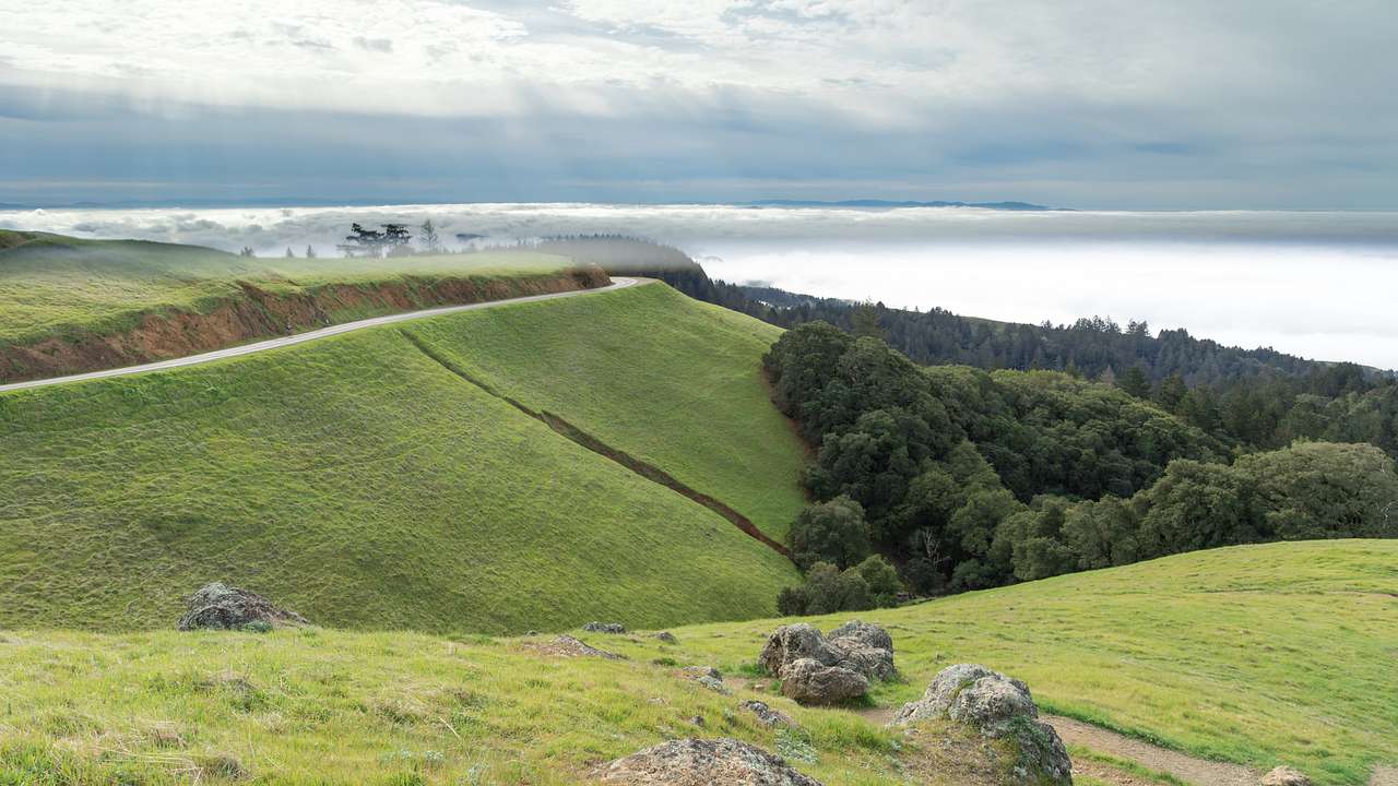 A green mountain with fog in front of it under a cloudy sky with sun rays
