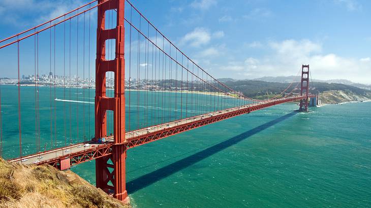 A red suspension bridge between two mountains with a body of water underneath