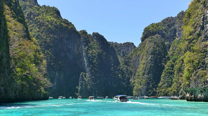 Tourist boats floating and moving on turquoise water surrounded by limestone cliffs