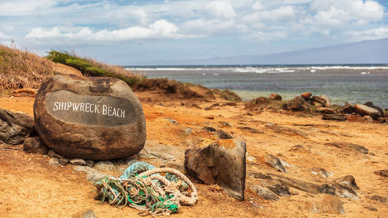 A beach with a rocky coastline and a rock engraved with the words "Shipwreck Beach"