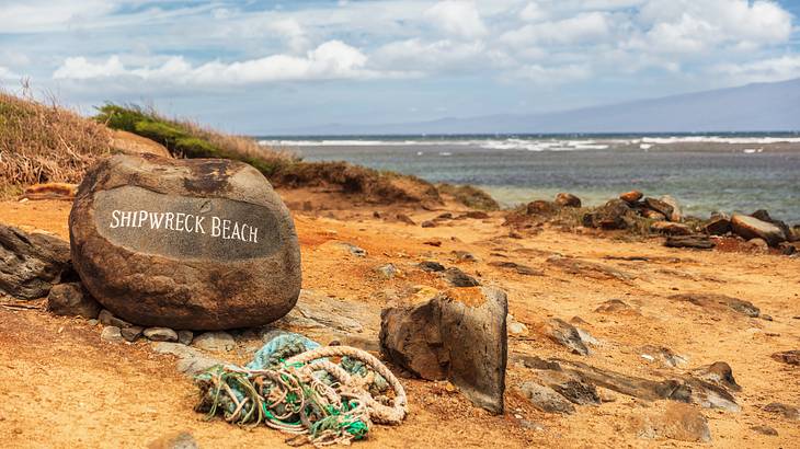 A beach with a rocky coastline and a rock engraved with the words "Shipwreck Beach"