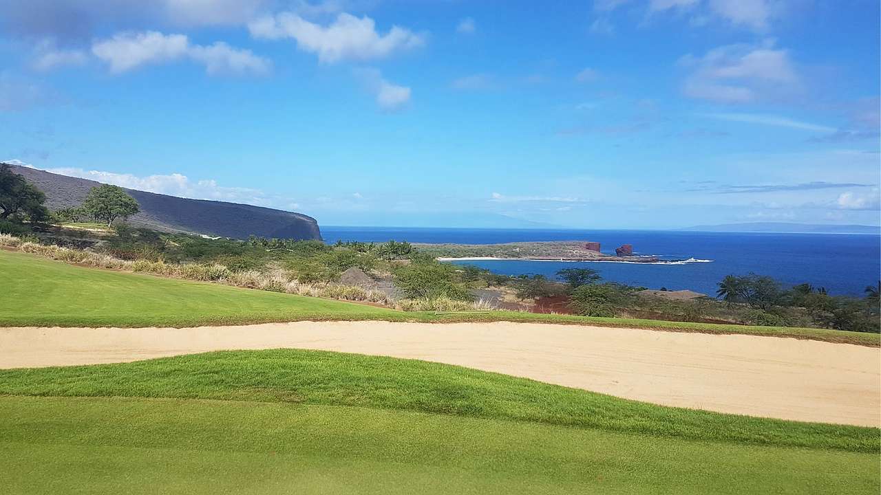 A golf course on a cliff next to the ocean under a blue sky with clouds