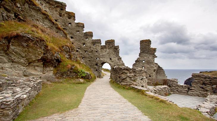 A dilapidated castle wall next to a path with grass on either side