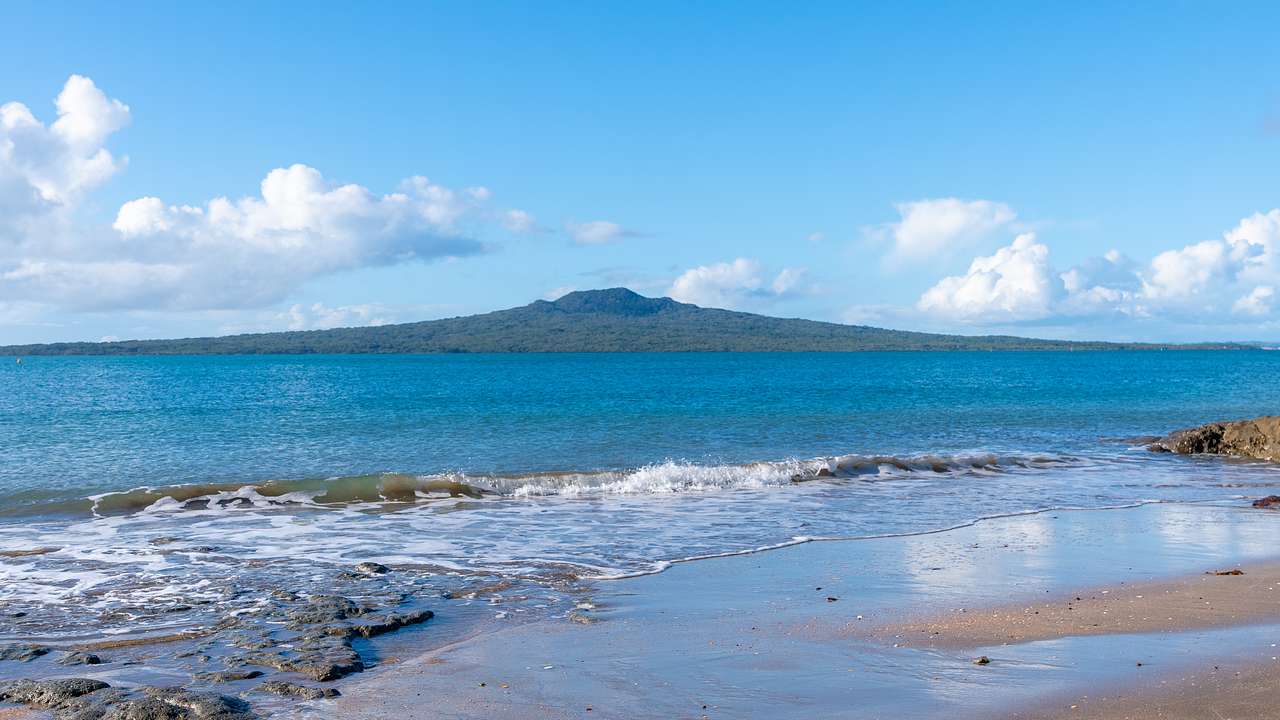 A mountain-like island next to the blue sea and a beach beneath a partly cloudy sky