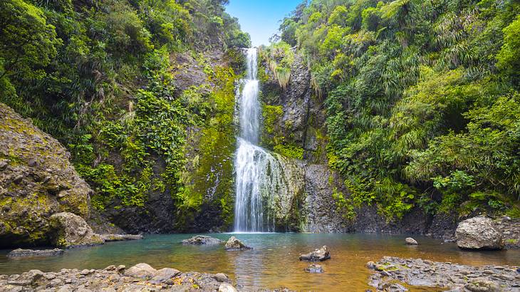 A three-tier waterfall cascading amidst a rocky landscape of green trees and shrubs