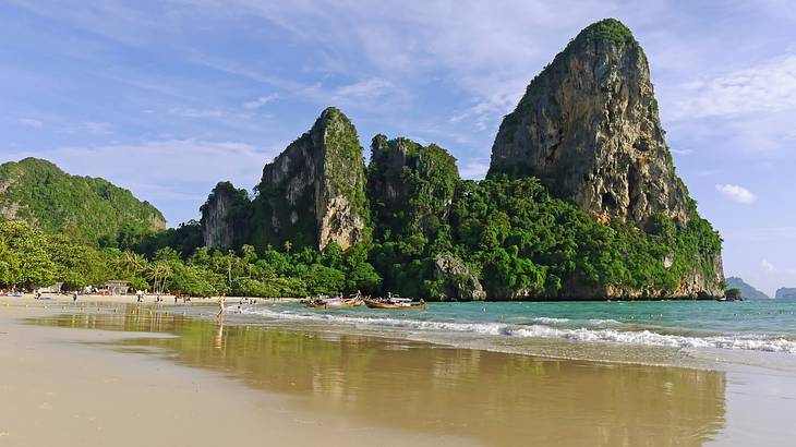 View of a beach with people, boats, and high limestone cliffs covered with trees