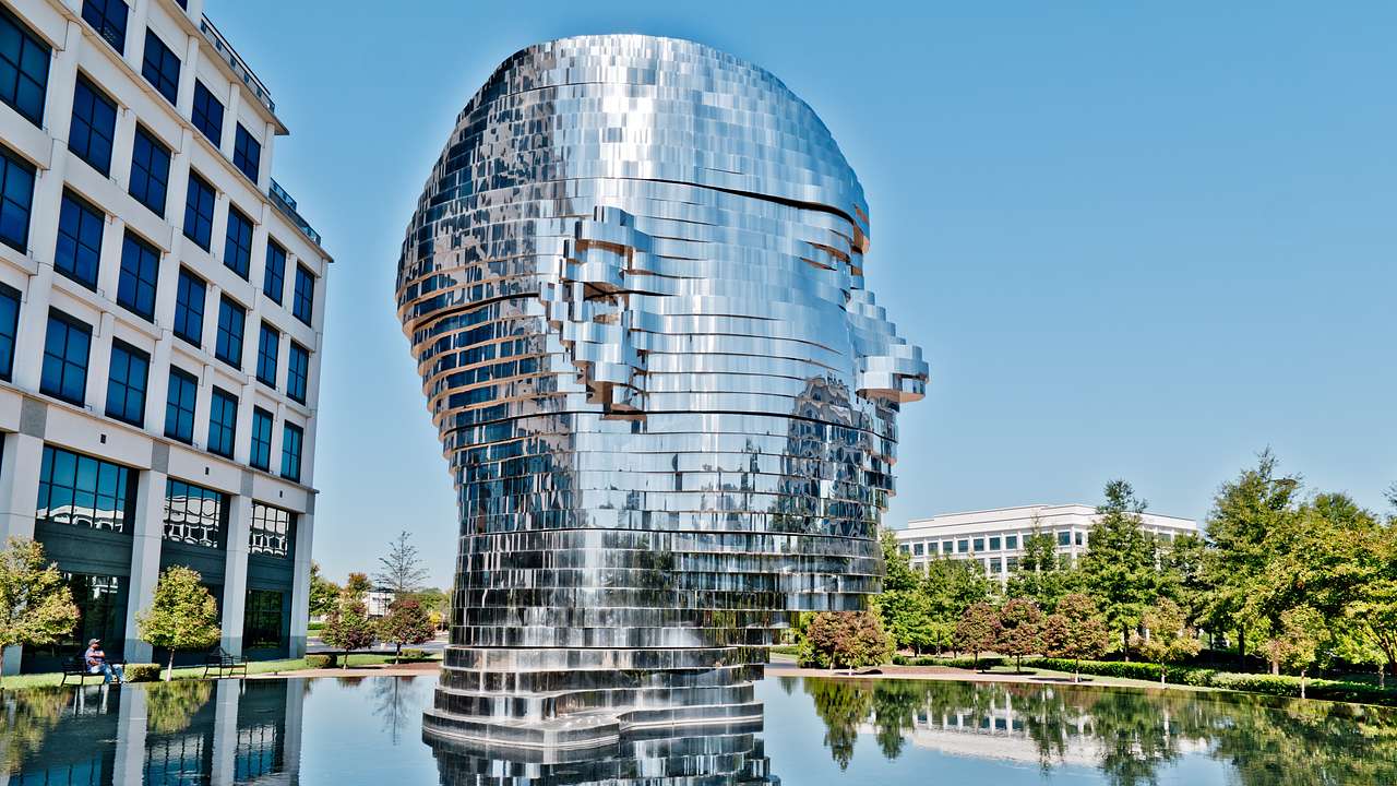 A modern metal sculpture of a human head next to a pool of water