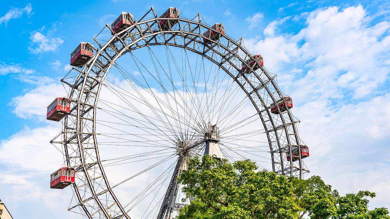 A giant Ferris wheel next to green trees under a blue sky with clouds