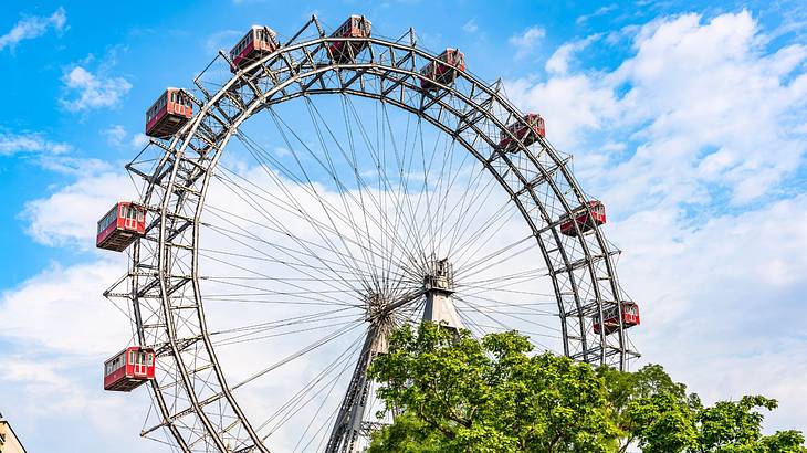 A giant Ferris wheel next to green trees under a blue sky with clouds