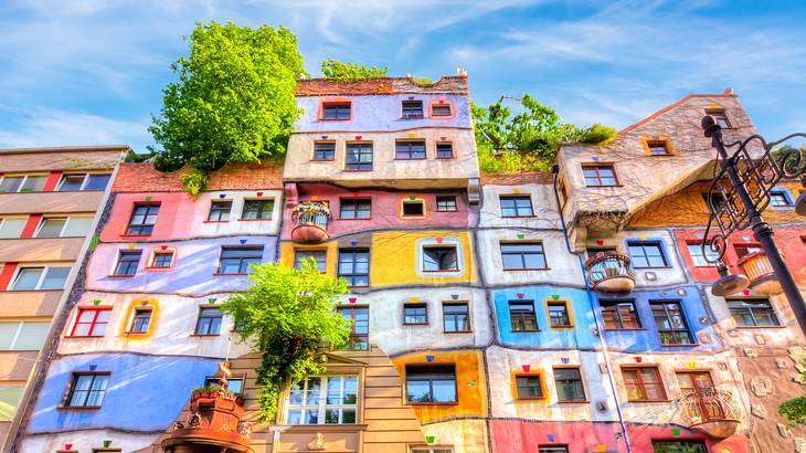 The facade of a colourful building with a few green trees, under a blue sky