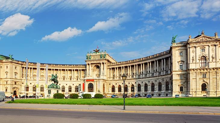 A panoramic view of a curved palace with a green lawn and cars parked in front