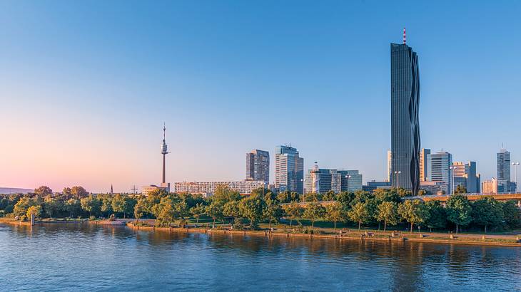 Cityscape with buildings and trees in the background and a blue river in front