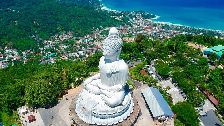 Aerial view of a big Buddha statue surrounded by trees, buildings, and the ocean