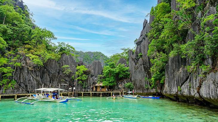 An emerald lake with a boat docked on it next to tall cliffs with greenery