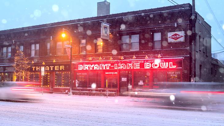 A building with a red, lit-up sign that says "Bryant Lake Bowl" facing a snowy road