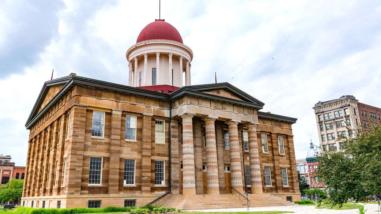 A neoclassical capitol building with a red dome, under a cloudy sky