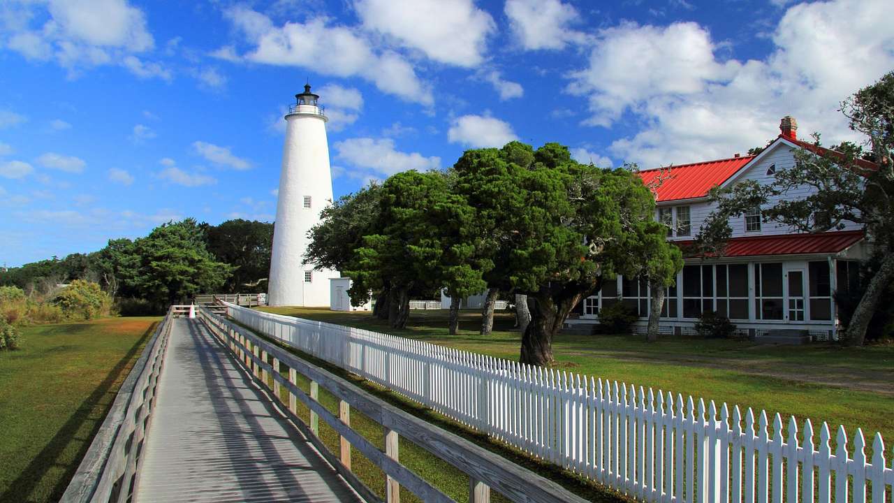 A long wooden walkway near fenced land with a house and a lighthouse at the end