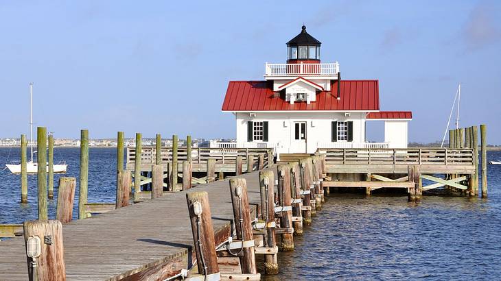 A small red and white building with a lighthouse next to water and a pier