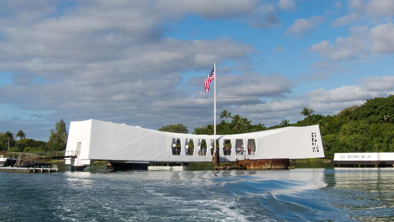 A white memorial building with an American flag in front of it, sitting on the water