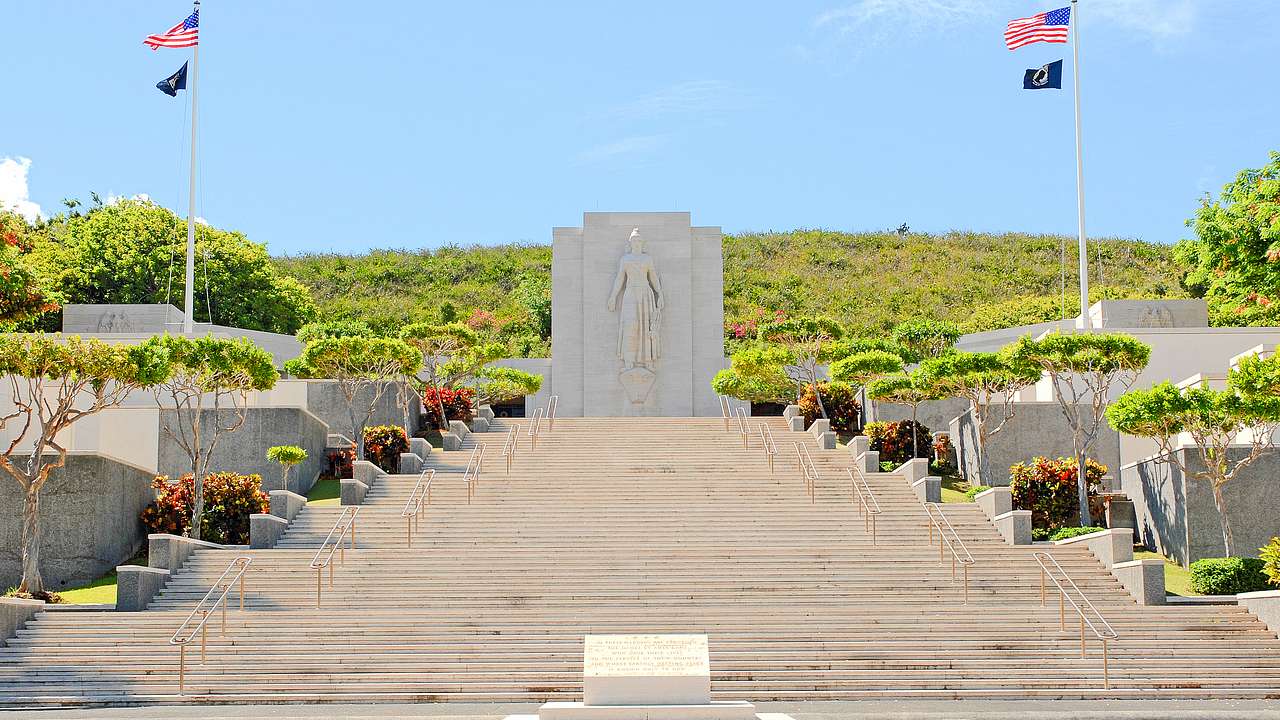 Steps leading up to a stone memorial with US flags and greenery surrounding