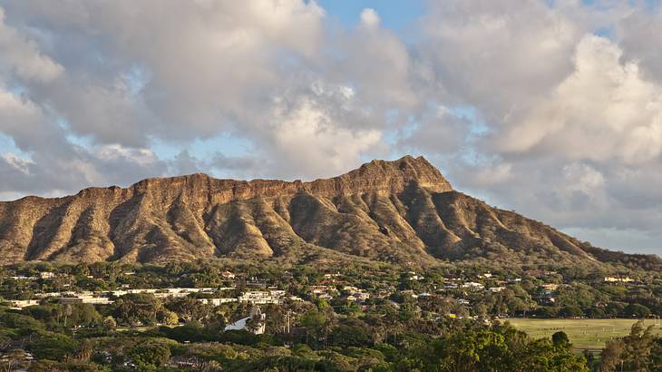 A volcanic mountain with greenery in front of it under a blue sky with clouds