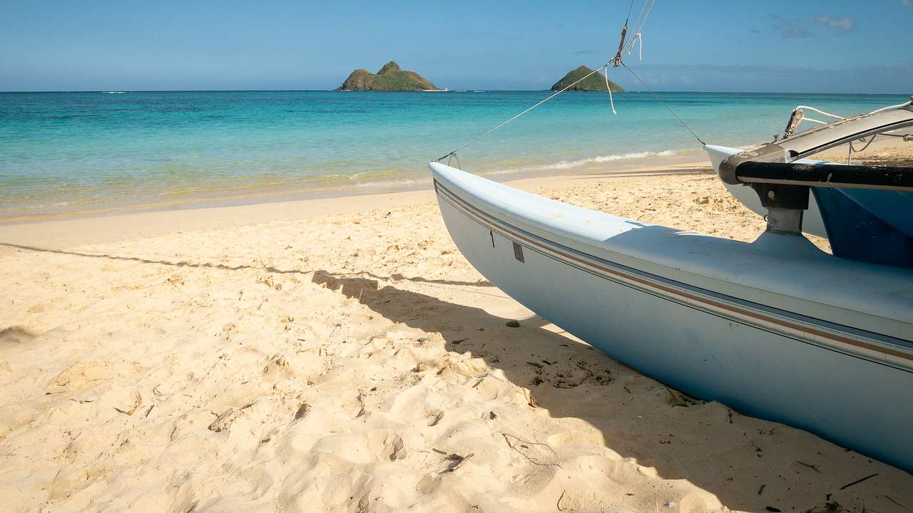 A boat lying on soft, white sand near the clear waters with islands at a distance