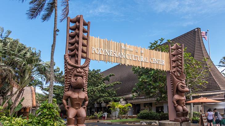 A straw sign with Polynesian statues and trees and buildings surrounding it