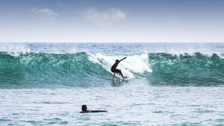 A surfer riding on a wave while another man swims to catch it