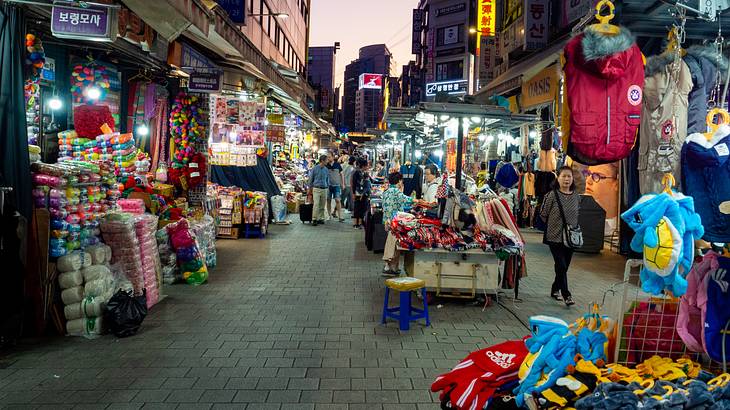 A street between buildings with people and stalls lined up selling various items