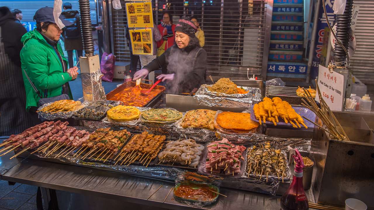 A person scooping food at a barbecue grill stall with many types of food laid out