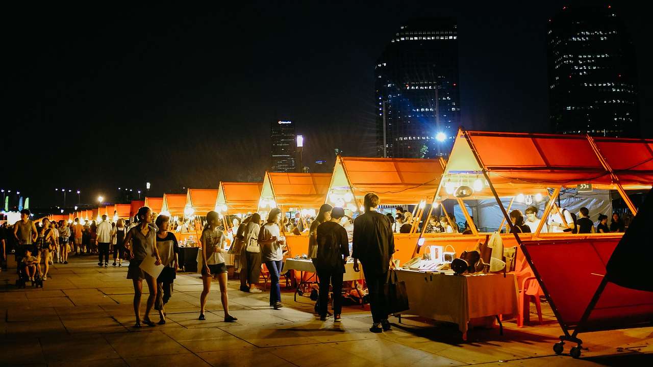 Red tents selling food in a large square with people wandering by at night