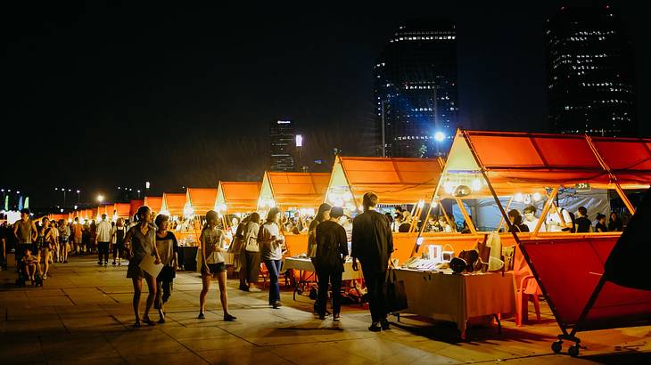 Red tents selling food in a large square with people wandering by at night