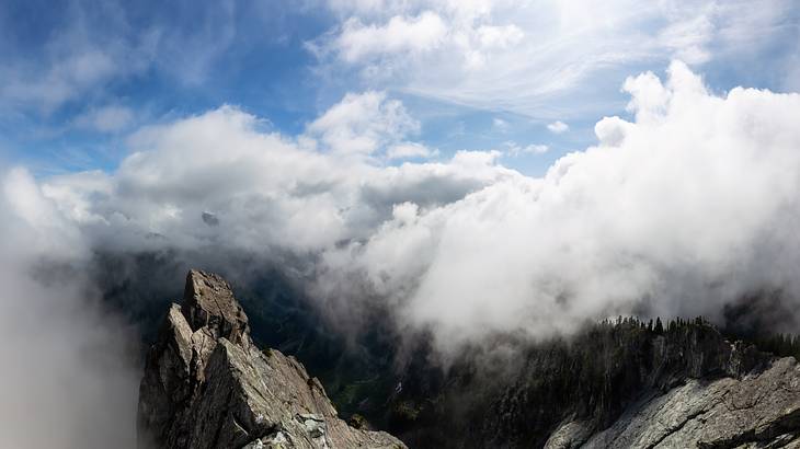 A rocky mountaintop surrounded by clouds with rocks and trees peeking through