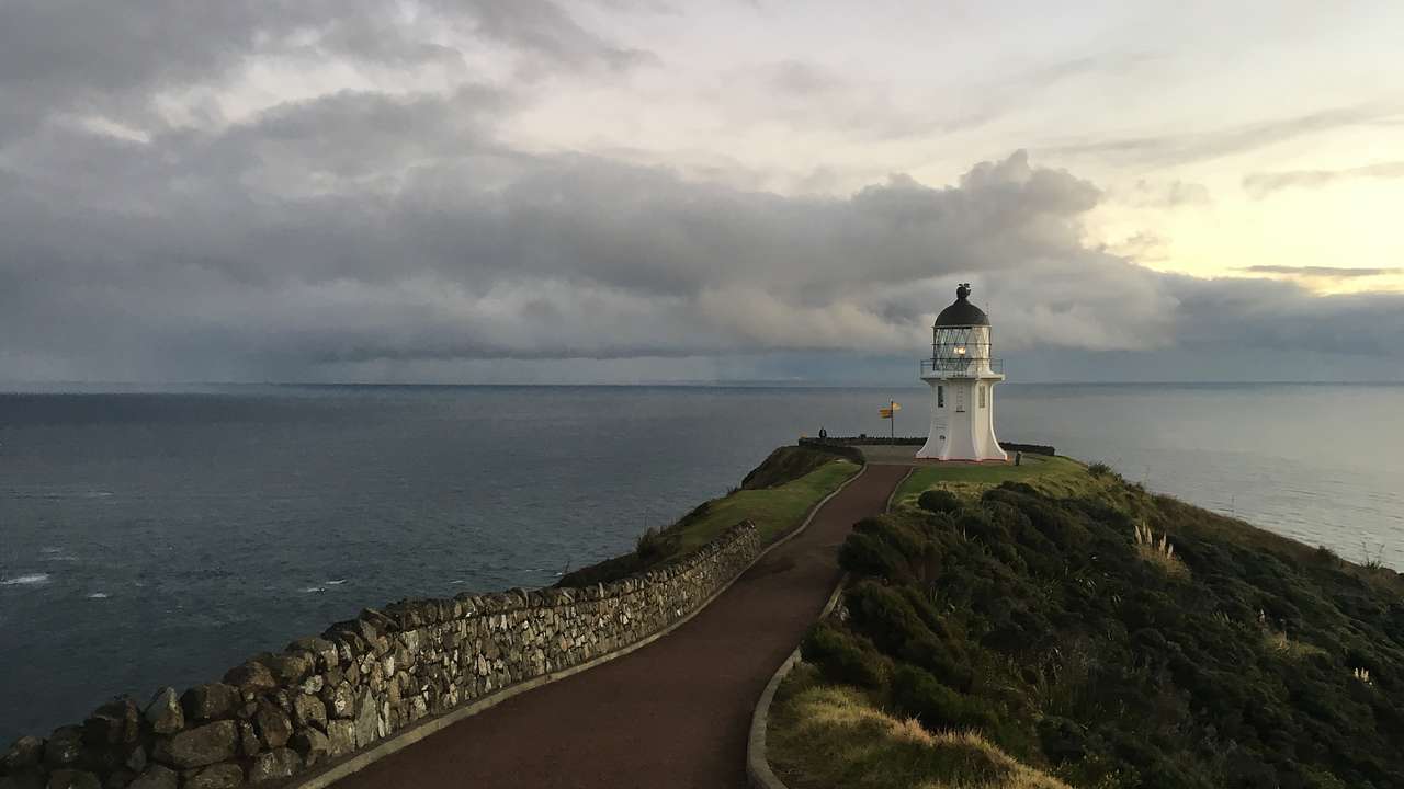 A lighthouse on a hill with a path leading to it surrounded by the ocean