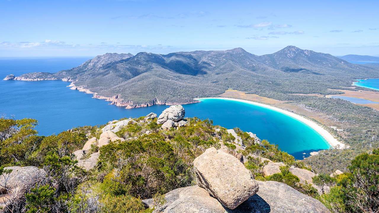 A crescent-shaped beach with white sand and blue waters amidst green mountains
