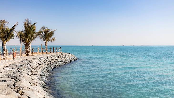 A stone pier with palm trees next to the blue ocean under a clear sky