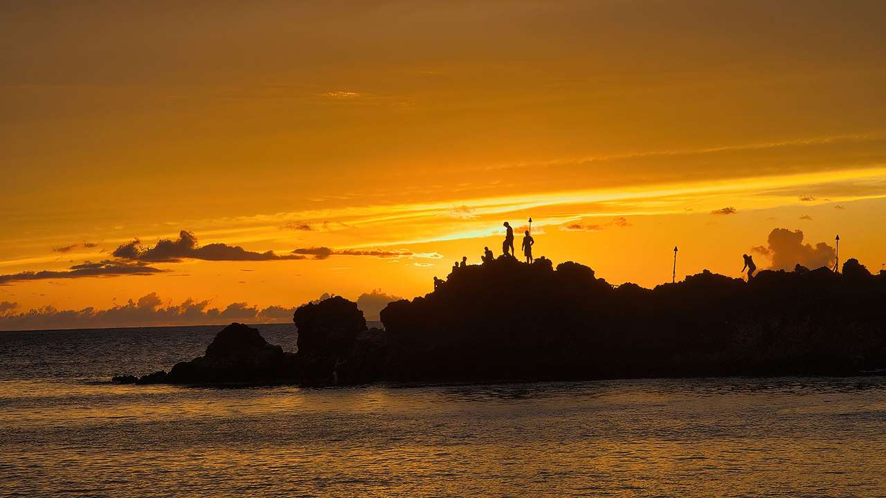 Silhouettes of people standing on the rocky landscape next to the ocean during sunset