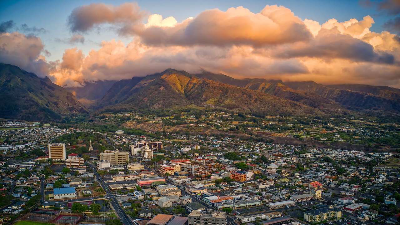 An aerial view of buildings and houses next to the mountains under sunset clouds