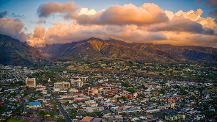 An aerial view of buildings and houses next to the mountains under sunset clouds