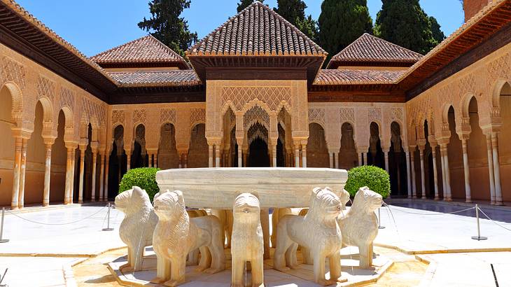 A white sculpture with a bowl and lions at its base next to an ornate building