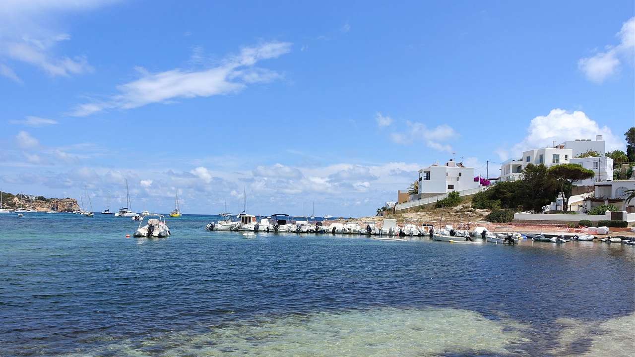 Ocean water near a hill with white houses on it under a blue sky