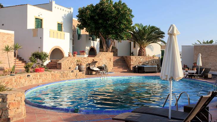 A swimming pool near stone short walls, sun loungers, and umbrellas