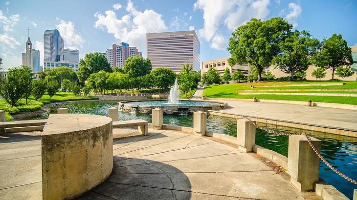 A park with a body of water and fountain with trees and buildings in the distance