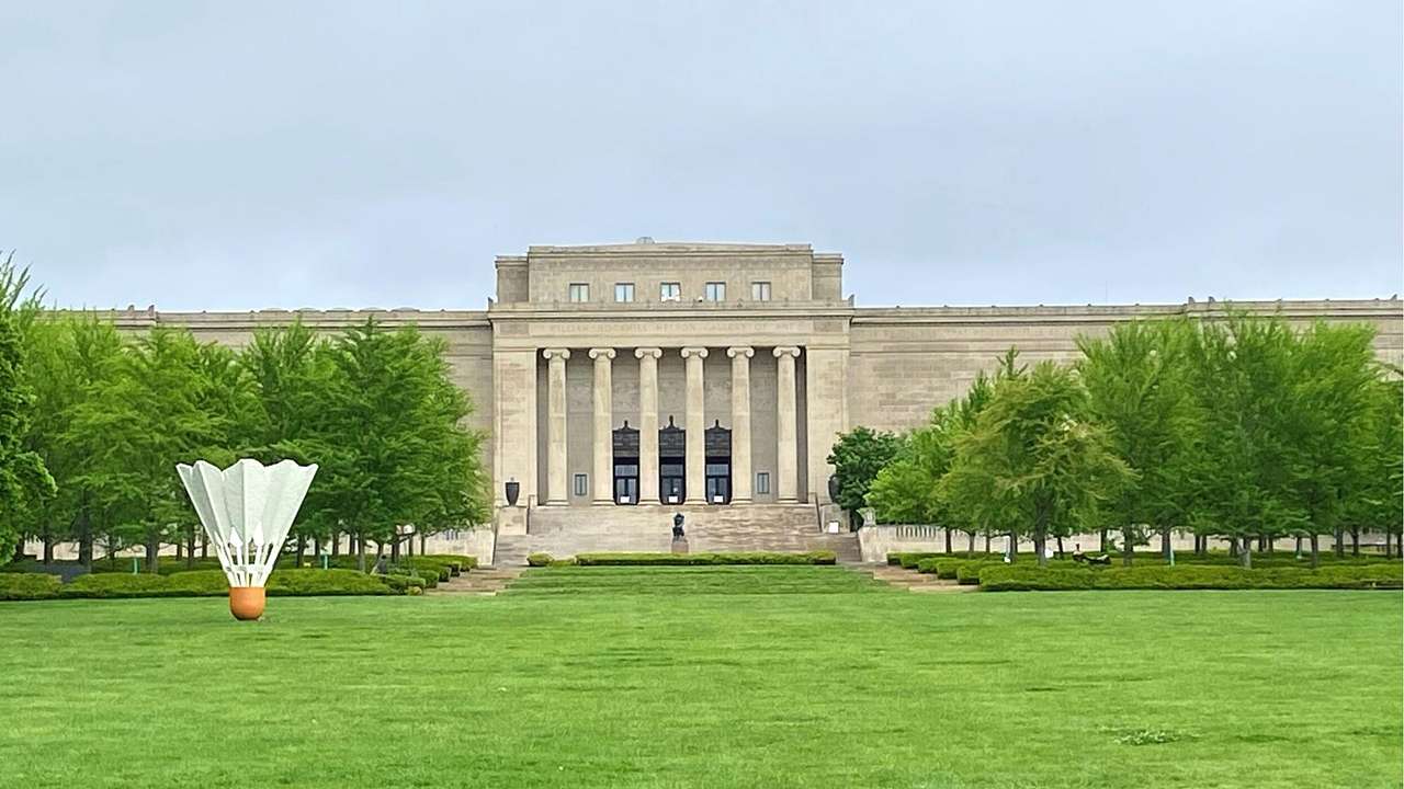 A neoclassical building with columns behind green grass with a shuttlecock sculpture