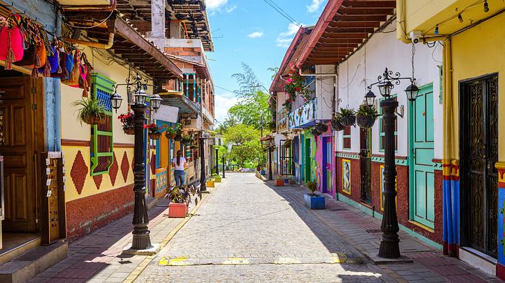 A small street with colourful buildings on either side and trees at the end