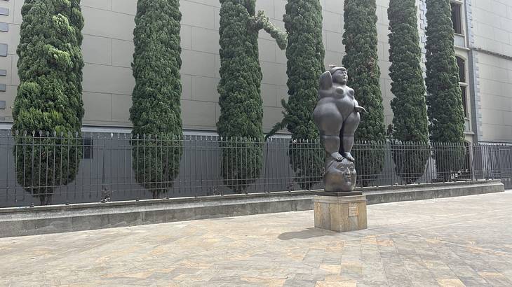 A plump statue of a woman in the middle of a courtyard with trees lined at the back